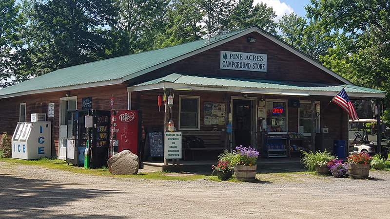 A small wooden campground store with vending machines, picnic tables, and flower planters out front